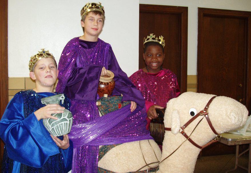 Three boys dress up as wisemen pose for a picture with their camel.