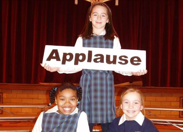 Children holding applause sign in Christmas: We're on the Air musical.